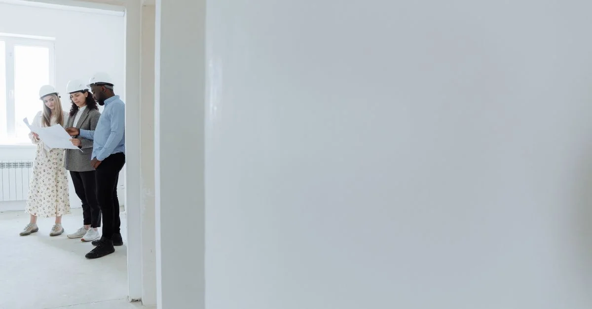 Des architectes portant des casques de sécurité examinent des plans à l'intérieur d'un bâtiment en construction.
