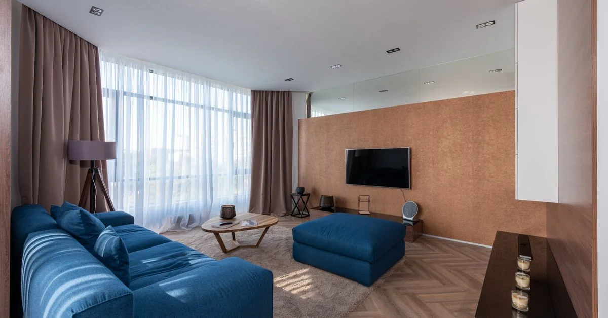 Salon moderne avec un canapé bleu, un pouf et de la lumière naturelle.