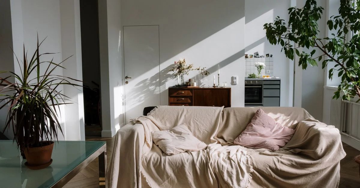 Intérieur d'appartement cosy baigné de lumière, avec un canapé confortable couvert de beige, des plantes en pot et une décoration chaleureuse.