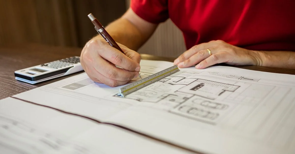 Architecte travaillant sur des plans de sol avec une règle et un crayon dans un bureau.