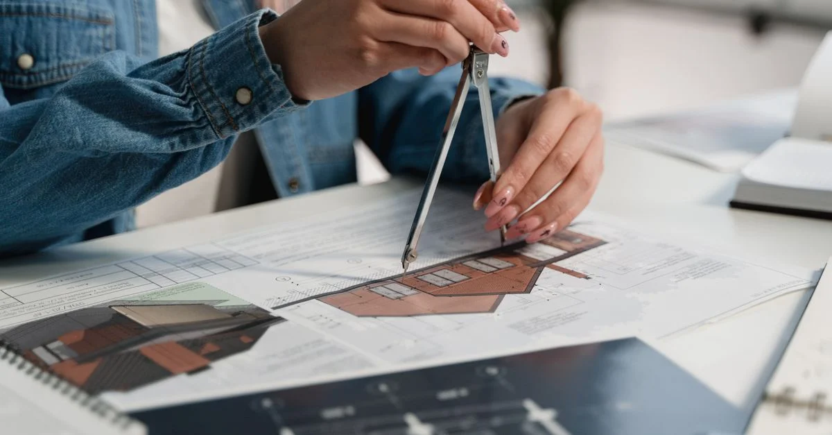 Un professionnel créatif utilisant une boussole sur des plans au bureau.