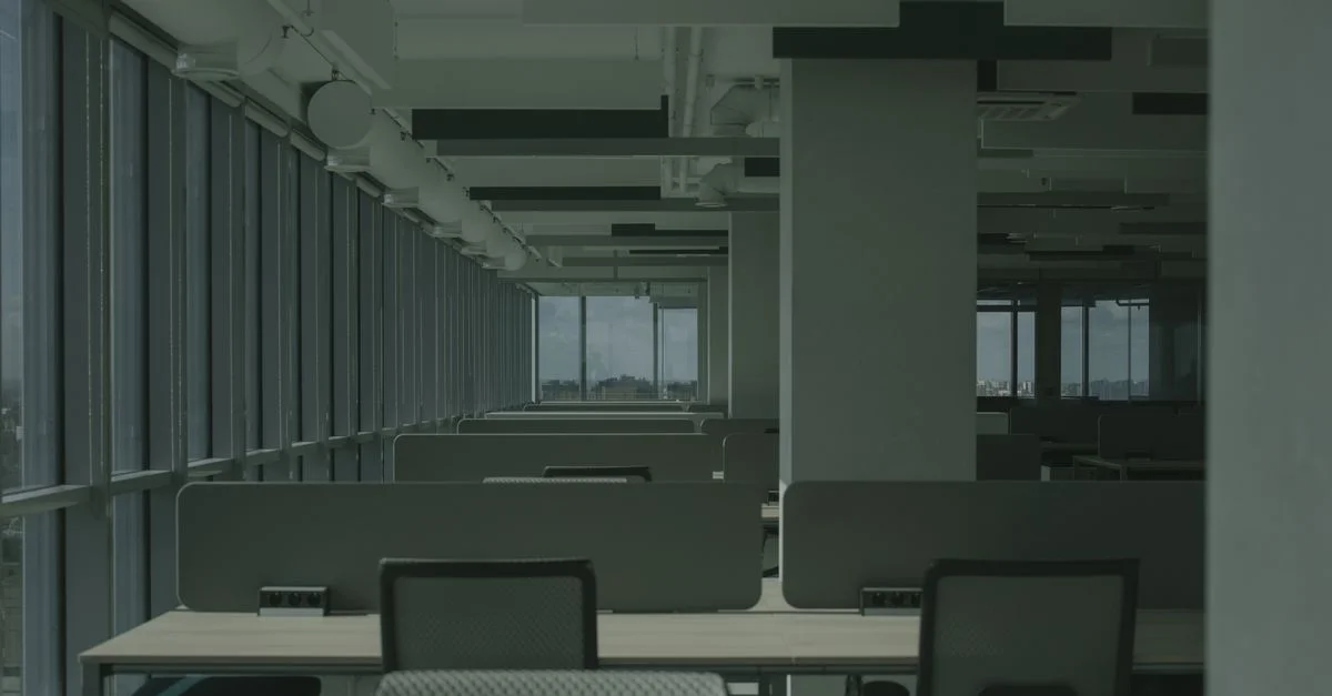 Bureau spacieux et vide avec des rangées de bureaux et de grandes fenêtres.