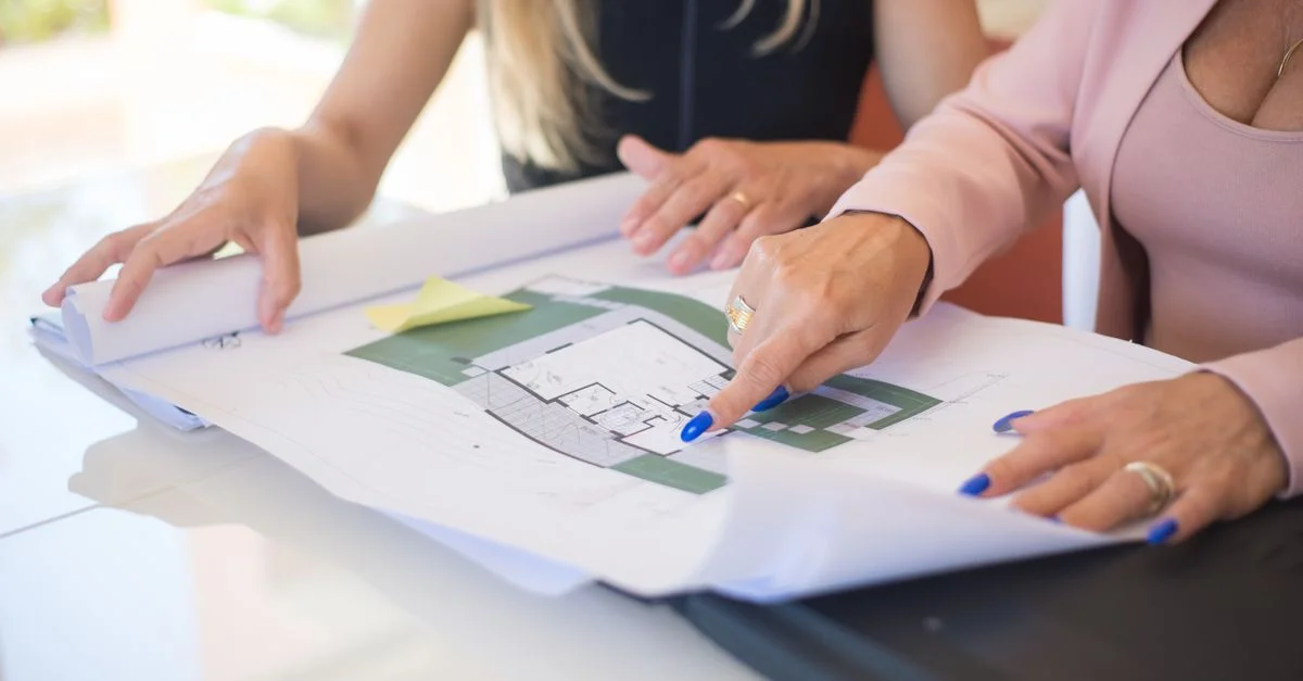 Deux femmes examinant des plans architecturaux détaillés dans un cadre professionnel.